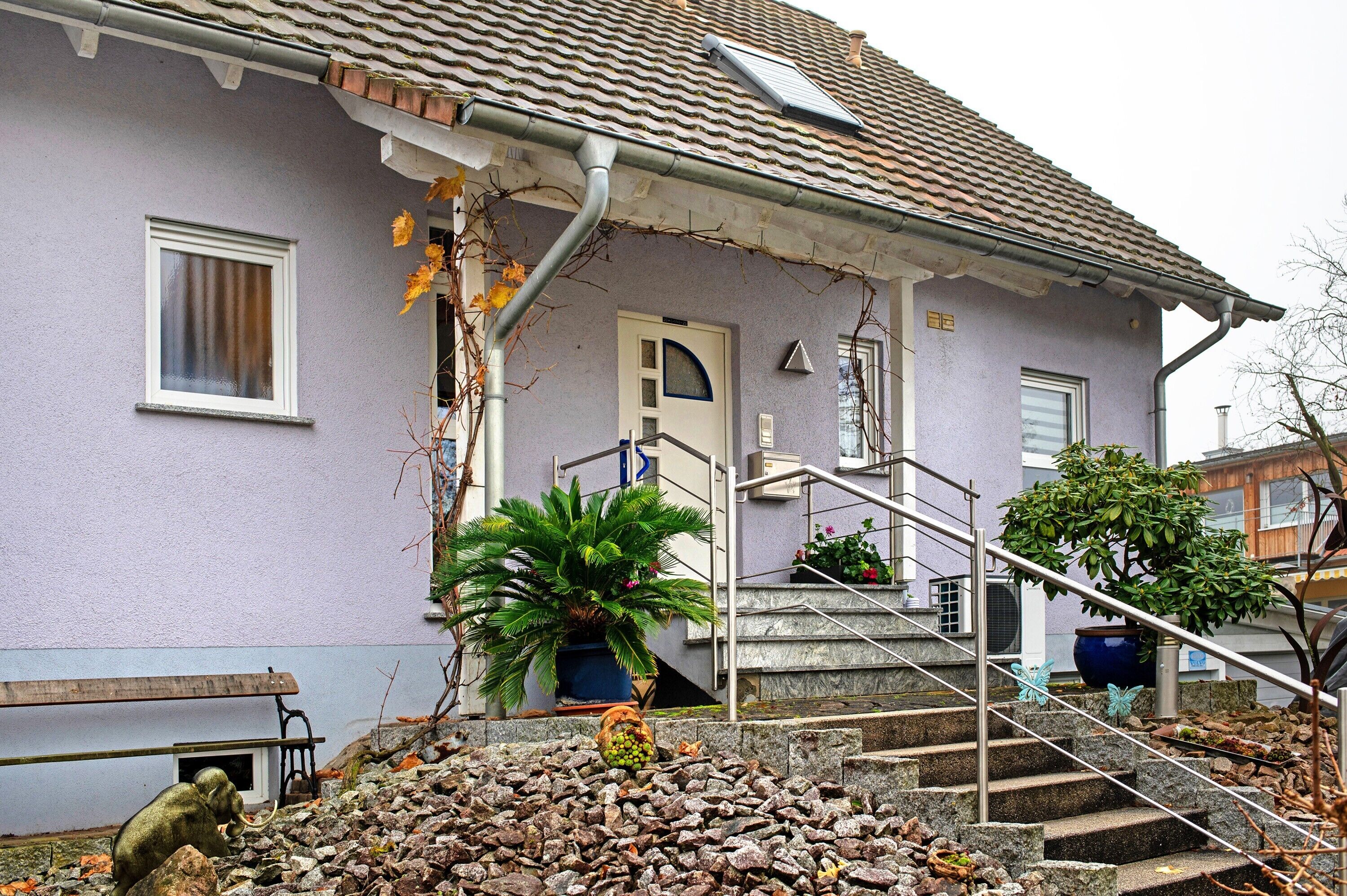 Una casa con techo de tejas, puerta principal, escaleras y una planta en maceta.