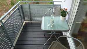 A balcony with a glass table, two chairs, a potted plant, and a bottle of water. - Holiday Apartment Mühlerain with Balcony (Heitersheim)