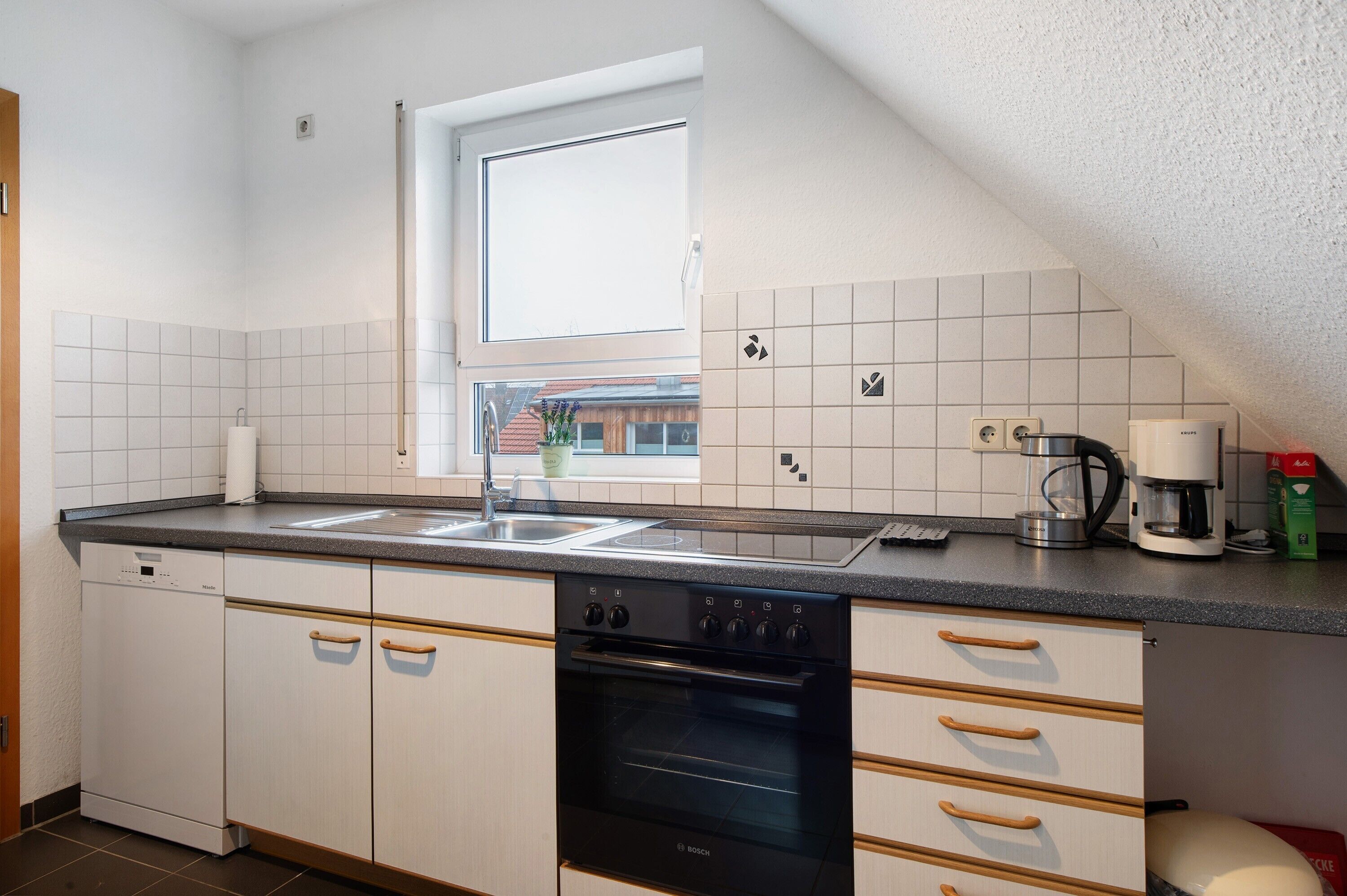 Una cocina con armarios blancos, un horno Bosch, una cafetera y un ventanal.