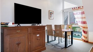 A room with a TV on a wooden cabinet, a dining table with chairs, a window with a view, and a staircase leading outside. - Holiday Apartment Mühlerain with Balcony (Heitersheim)