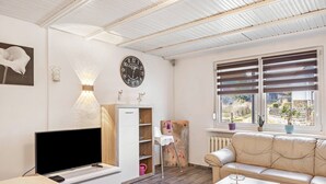 Una sala de estar moderna con un televisor de pantalla plana, un sofá, una mesa de centro, un reloj y una ventana con persianas.