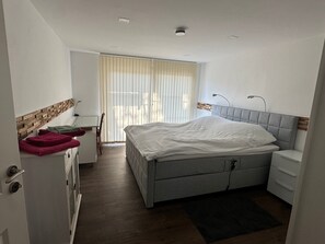 A bedroom with a bed, bedside table, lamp, and a view of the outside through a window.