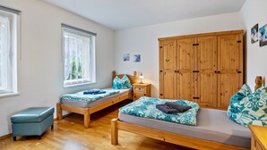 A room with two wooden beds, a small stool, a wooden wardrobe, and a window with curtains.