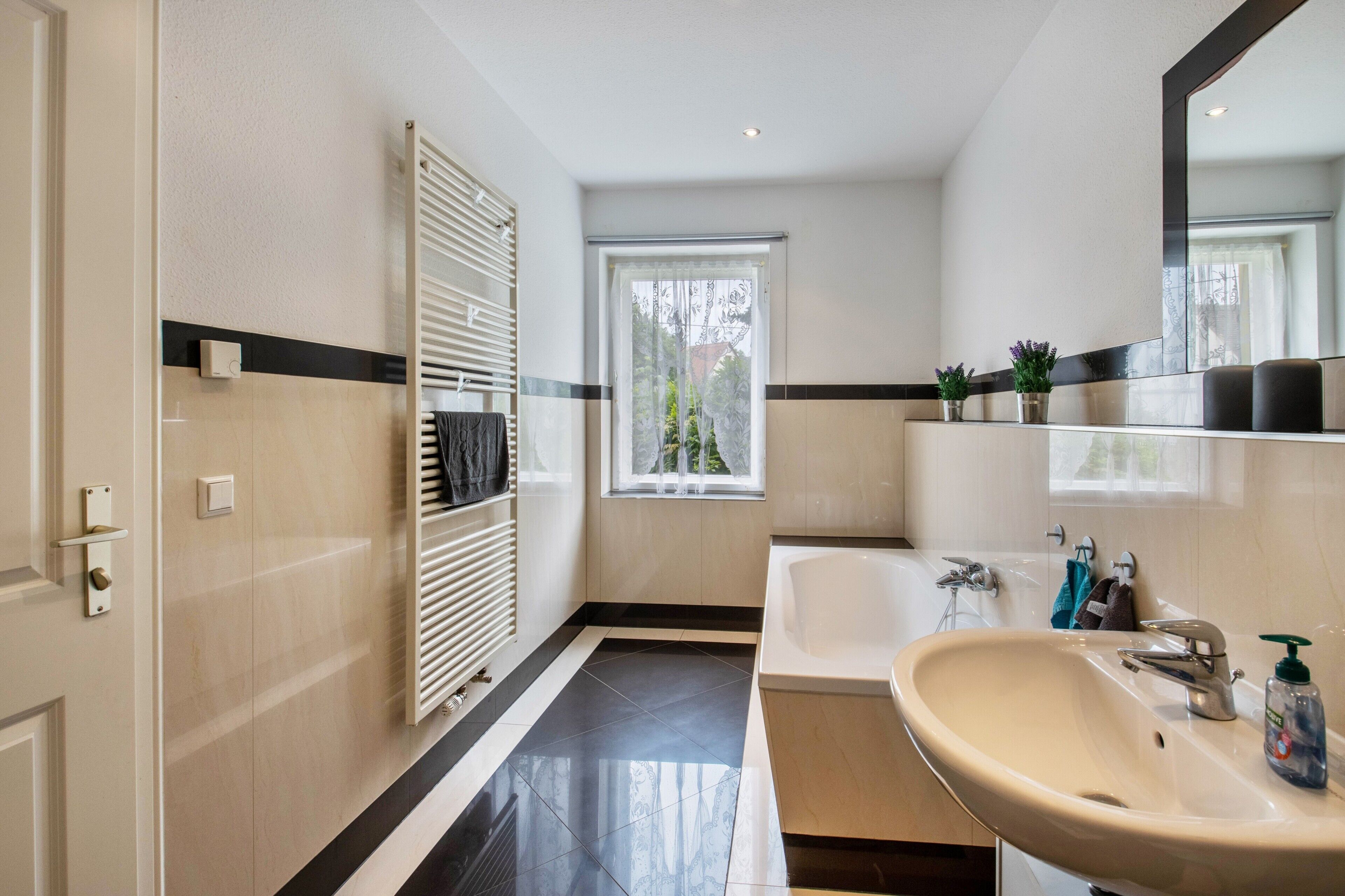 A modern bathroom with a bathtub, a sink, a window, and a towel rack.