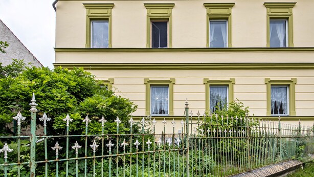 A two-story building with a symmetrical facade, evenly spaced windows, and a green metal fence with decorative elements.