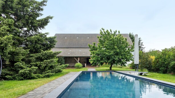 A rectangular swimming pool with a paved edge, surrounded by grass and trees, with a house in the background. - Farmstead 'Vierseitenhof' with Private Pool, Private Terrace and Wi-Fi (Ziesar)