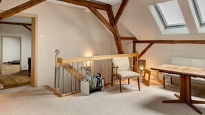 A loft bedroom with a wooden ceiling, skylights, a built-in bookshelf, a dining table, and a cushioned bench. - Farmstead 'Vierseitenhof' with Private Pool, Private Terrace and Wi-Fi (Ziesar)