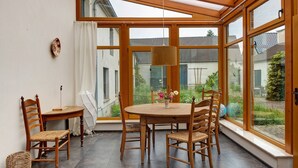A dining area with a round table, wooden chairs, a hanging light fixture, and large windows offering a view of the garden. - Farmstead 'Vierseitenhof' with Private Pool, Private Terrace and Wi-Fi (Ziesar)