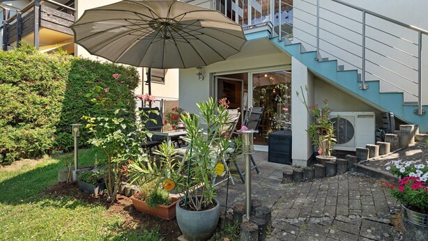 Un patio con plantas en macetas, un paraguas grande y una escalera que lleva a un balcón.