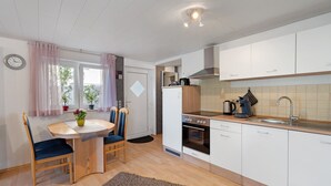 Una cocina moderna con armarios blancos, horno empotrado y un lavamanos. Hay una mesa de comedor con sillas y una pequeña alfombra en el suelo.