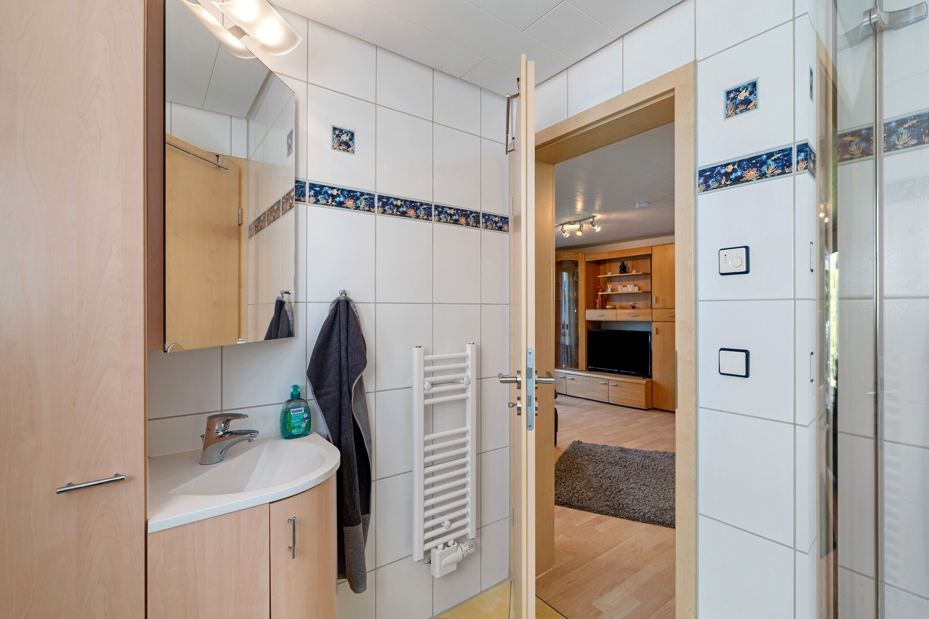 A bathroom with a sink, mirror, towel rack, and a shower area.