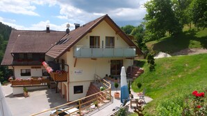 Ein zweistöckiges Gebäude mit Balkon, Außenbestuhlung und einem kleinen Garten.