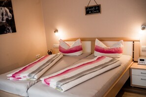 Una cama con ropa de cama a rayas, dos almohadas, una mesita de noche con una radio y un cartel en la pared.