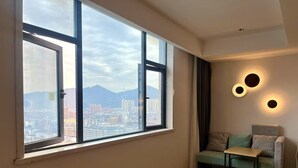 A room with large windows offering a city view, a sofa with cushions, and a small table. - Campanile Jingdezhen Mperial Kiln Hotel (Jingdezhen)