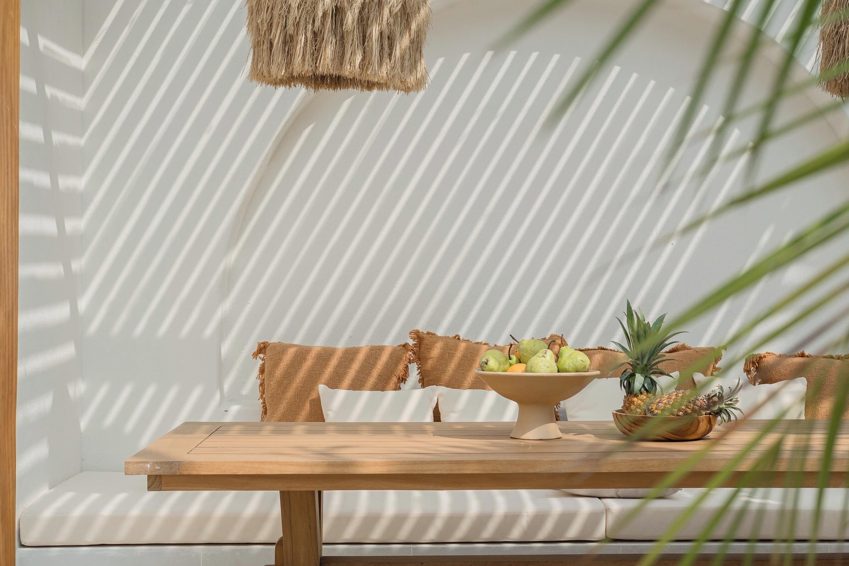 A wooden table with a bowl of fruit in front of a white sofa with striped cushions.
