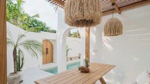A wooden table with a pineapple centerpiece, white walls, and a pool in the background.