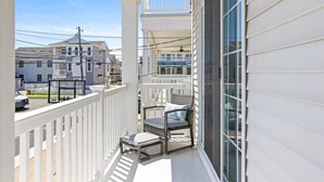 Un balcon avec une balustrade blanche, une porte vitrée et une chaise avec des coussins.