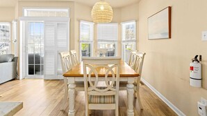 Un coin repas avec une table en bois et des chaises blanches, un luminaire suspendu et un extincteur fixé au mur.
