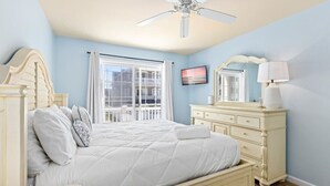 Une chambre à coucher avec un lit, une commode, un ventilateur de plafond, une fenêtre avec des rideaux et un tableau au mur.