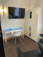 Een kamer met een bureau, stoel, kledingkast en een aan de muur bevestigde televisie.