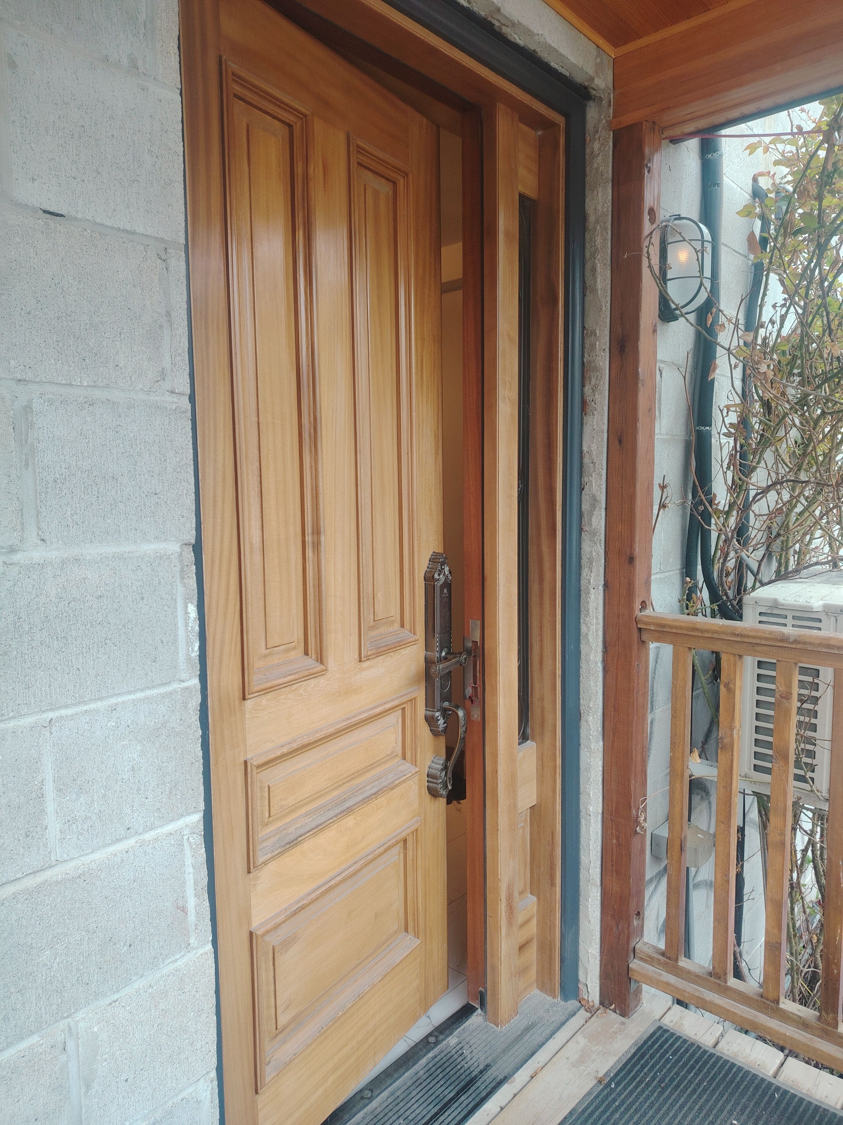 A wooden door with a metal handle and a small step leading to a balcony with a railing.