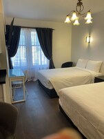 Habitación de hotel con dos camas, un escritorio, una silla y una ventana con cortinas.