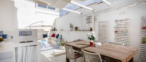 Una cocina y comedor integrados y luminosos, con una mesa de madera, armarios blancos y vistas al cielo.