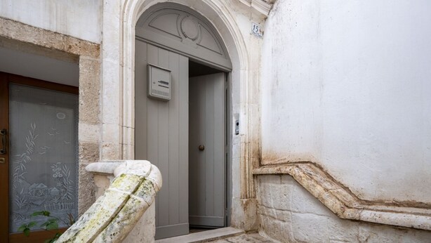 A building entrance with a stone staircase, a door with a number plate, and a wall with a decorative frieze. - GuestHost - Charming apartment of about 35 sqm, perfect for 2 people, located on the second floor of a building without a lift.The property is located in the heart of the historic center of Monopoli, a few steps from the splendid Cathedral of Santa Maria (Monopoli)
