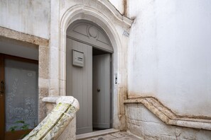 Entrada de un edificio con una escalera de piedra, una puerta con placa de número y un muro con un friso decorativo.
