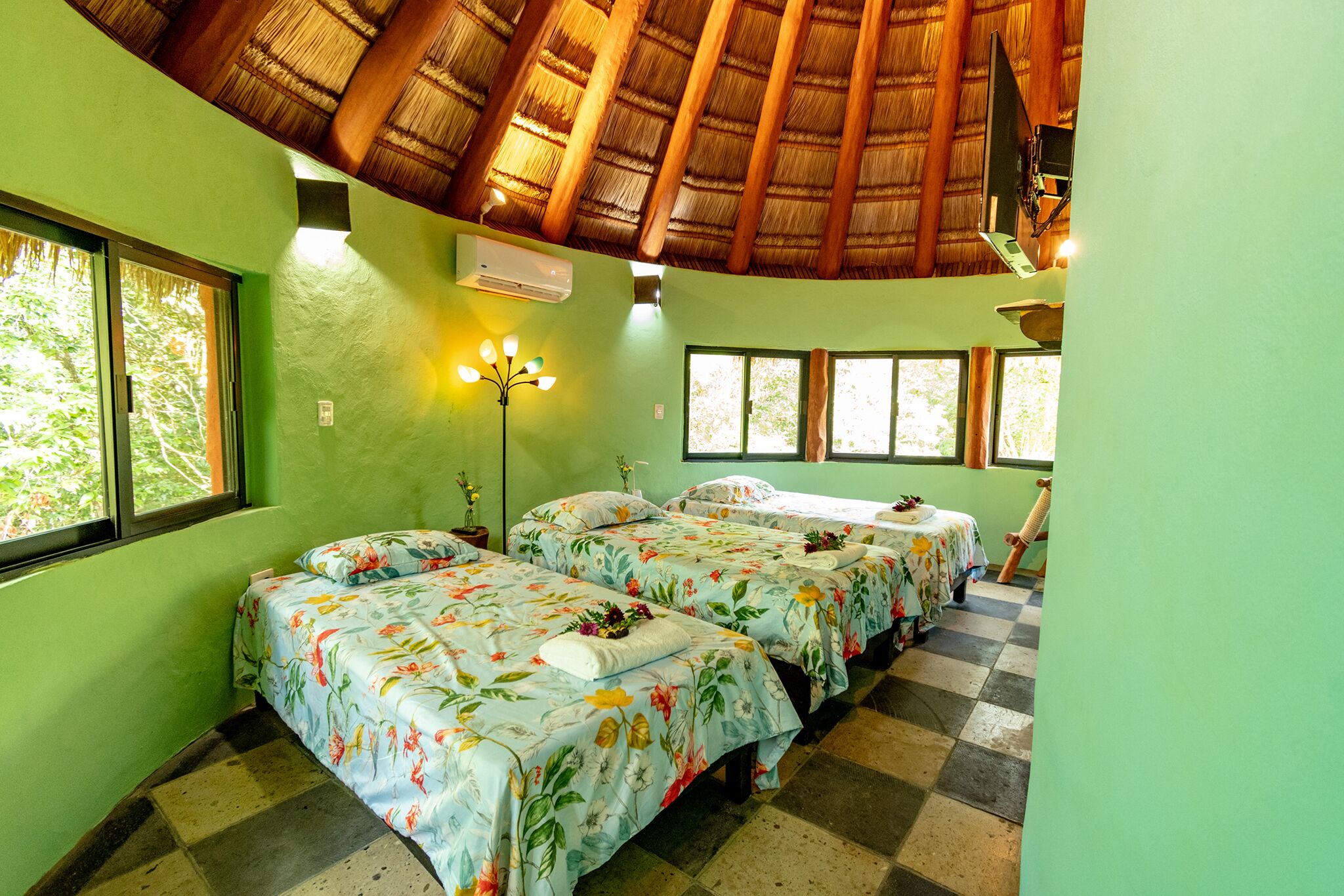 A room with three beds, a thatched roof, and a large window.