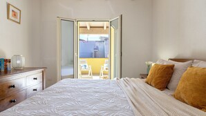 A bedroom with a large bed, a wooden dresser, and a balcony with chairs.