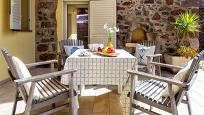 A patio with a stone wall, a table with a checkered tablecloth, chairs, a potted plant, and a small fireplace.