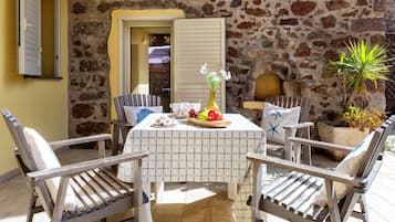 Une terrasse avec un mur en pierre, une table recouverte d’une nappe à carreaux, des chaises, une plante en pot et une petite cheminée.