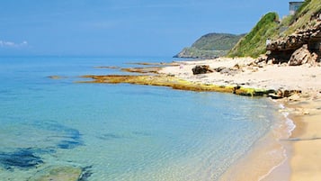 Une plage à l’eau claire, avec un rivage sablonneux et un bâtiment perché sur une falaise.