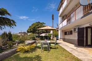 A patio with a table and chairs, a large umbrella, and a view of a building with a balcony.
