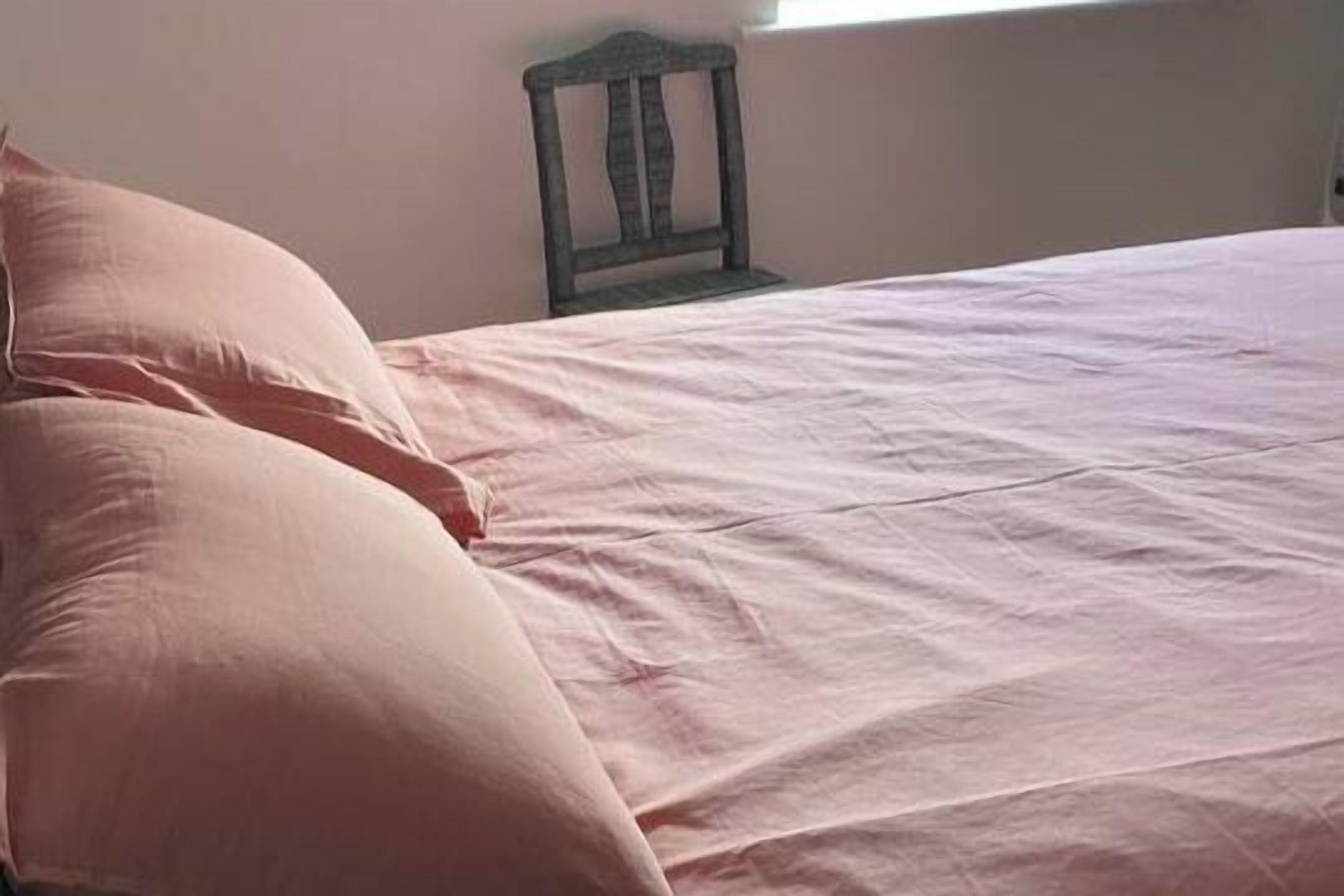 Un lit avec une couvre-lit rose et deux oreillers.
