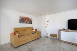 Una sala de estar moderna con un sofá, un cuadro, una lámpara de pie, un banco y un televisor sobre un mueble de madera.