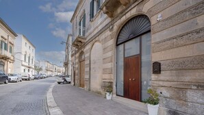 A street view with a building featuring a large wooden door, stone facade, and potted plants. - GuestHost - Dimora Marseglia (Ostuni)