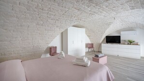 A bedroom with a sloped ceiling, a bed, a TV, a dresser, and a small seating area. - GuestHost - Dimora Marseglia (Ostuni)