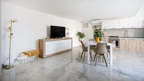 A modern kitchen with white cabinets, a dining area with a white table and chairs, and a TV on a wooden cabinet. - GuestHost - Dimora Marseglia (Ostuni)