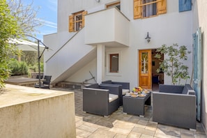 Un patio moderno al aire libre con mobiliario de mimbre, una escalera y una puerta que da a un espacio interior.