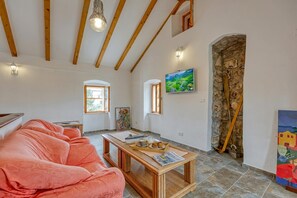 A cozy room with a wooden ceiling, a sofa, a table with a tray, a painting, and a stone wall.