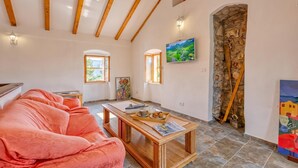 A cozy room with a wooden ceiling, a stone wall, a wooden table with a tray of food, and a colorful painting. - Casa Lussingrande Island Retreat with Terrace, Veli Lošinj, Croatia (Veli Lošinj)