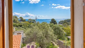 A view through a window of a coastal area with trees, a clear sky, and a distant view of the sea. - Casa Lussingrande Island Retreat with Terrace, Veli Lošinj, Croatia (Veli Lošinj)
