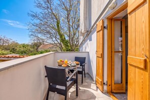 Un balcón con una mesa lista para el desayuno, dos sillas de mimbre y una puerta de madera.