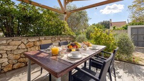 An outdoor dining area with a stone wall, wooden pergola, and a table set with breakfast. - Casa Lussingrande Island Retreat with Terrace, Veli Lošinj, Croatia (Veli Lošinj)