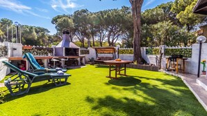 Un jardin avec un espace barbecue, une table et des chaises longues.