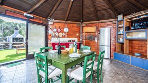 Une cuisine ouverte sur la salle à manger, avec un plafond en bois, une table à manger pour quatre personnes et un réfrigérateur.
