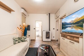 A compact living space with a sofa, a coffee table with a vase, a television, a fireplace, and a view of a lake through a window. - La Rosa dei Venti, Sorso, Italy (Sorso)