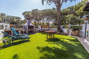 A backyard with a grill, lounge chairs, and a table.